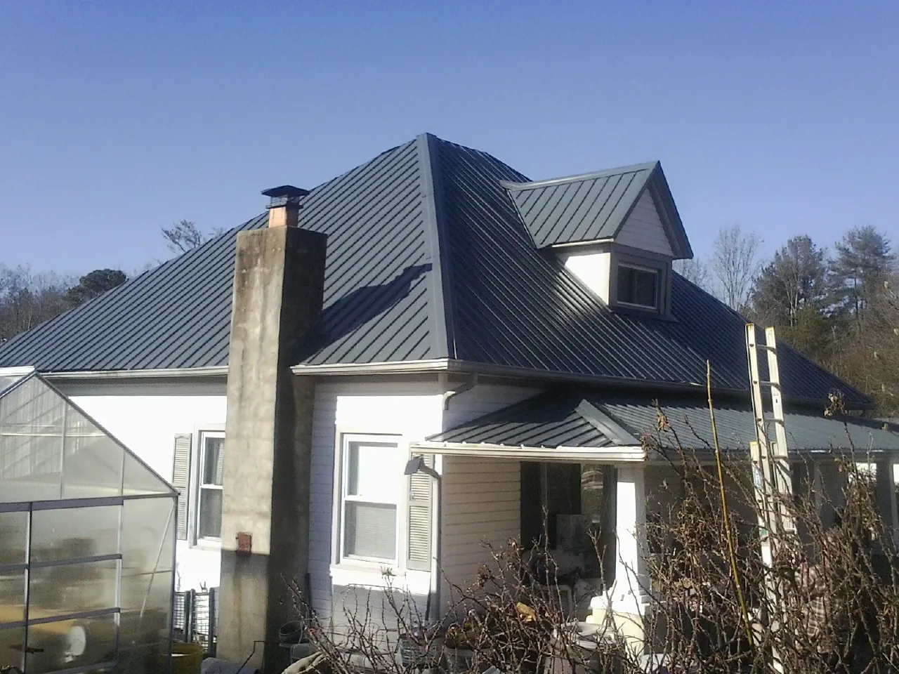 Dark blue standing seam metal roof on a white farmhouse with dormer — Slate & Tile Roof Repair by Roofing Brothers in Weskan
