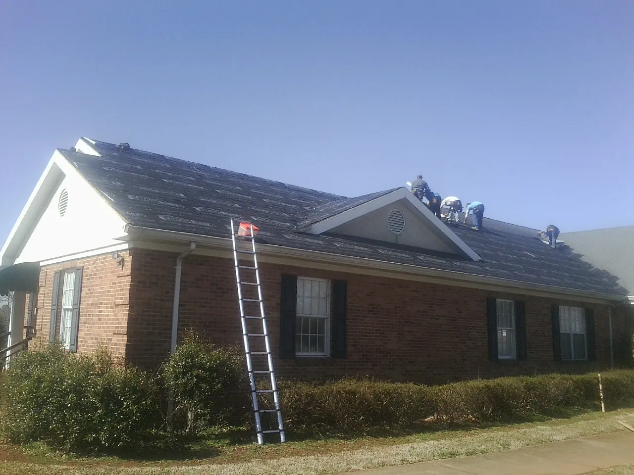 Crew tearing shingles off a brick ranch roof with a ladder set — Emergency Roof Repair work by our crew in Weskan