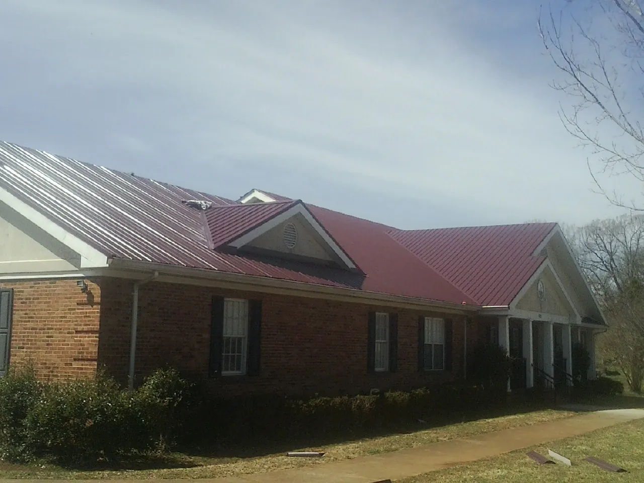 Red metal roof with gabled entries on a long brick building, from a Hail Damage Roof Repair job in Weskan