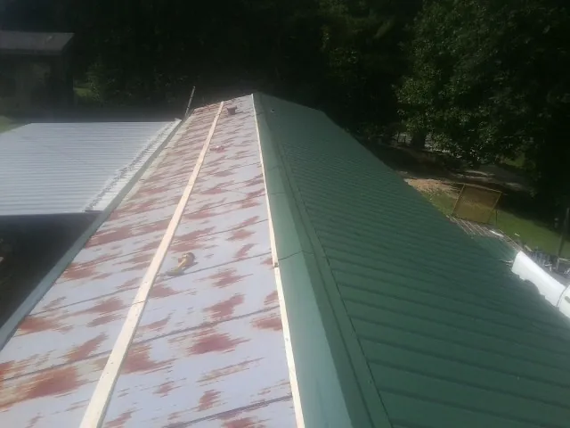 Old rusted panels beside newly installed green metal roofing — Wind Damage Roof Repair by Roofing Brothers in Weskan