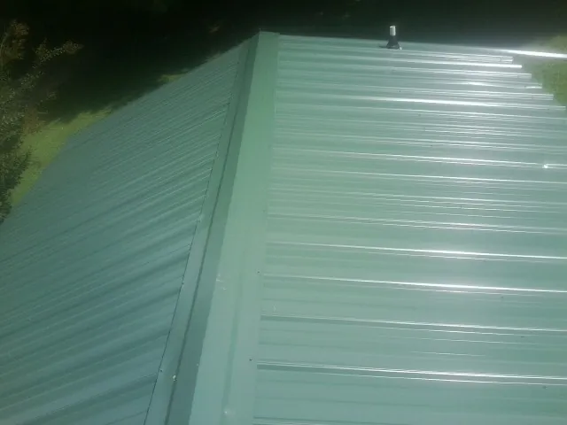 New green metal panels meeting at the ridge of a roof — Flat Roof Repair work by our crew in Weskan