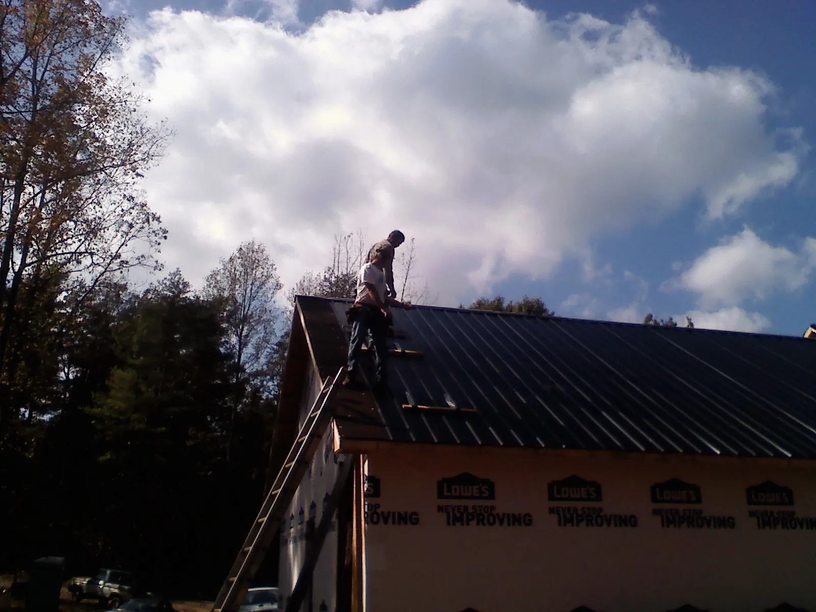Roofer fastening dark metal panels high against a cloudy sky, from a Roof Inspection job in Weskan