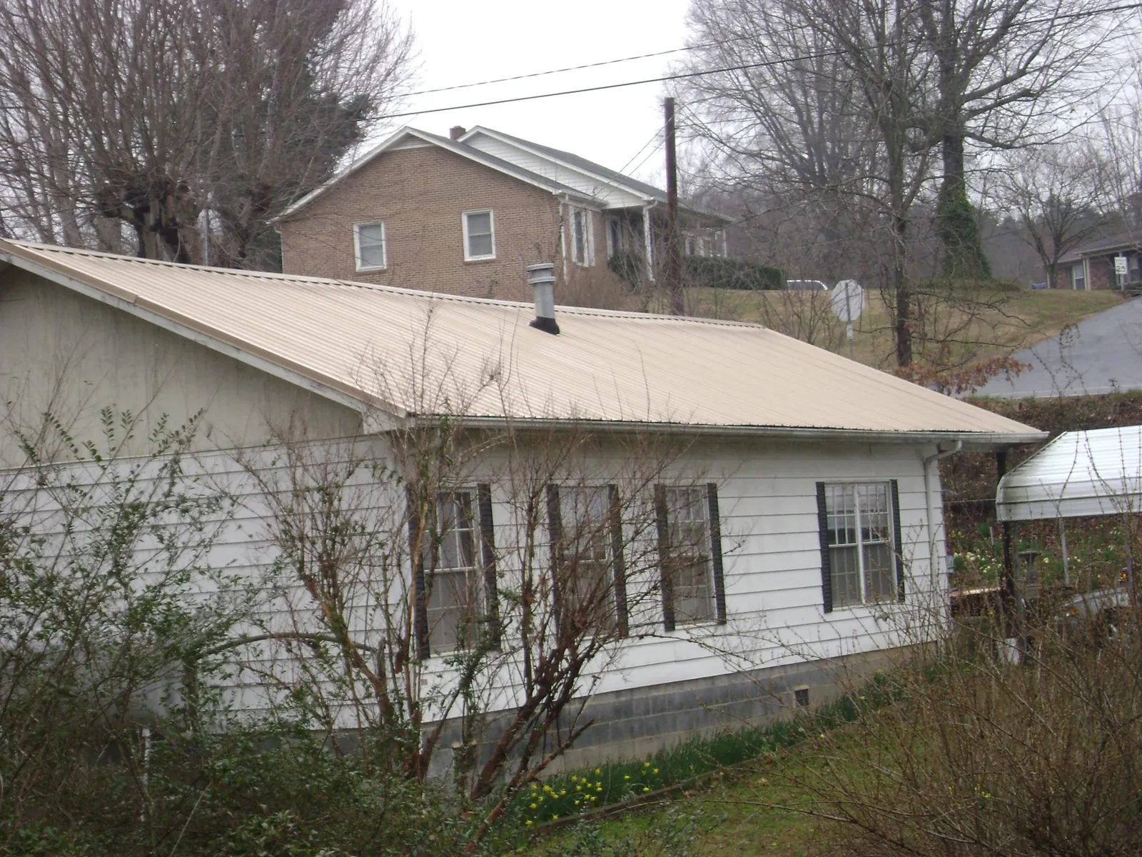 Tan metal roof on a white sided house set into a hillside — Commercial Roofing by Roofing Brothers in Weskan